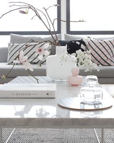 a living room filled with furniture and flowers on top of a coffee table in front of a window