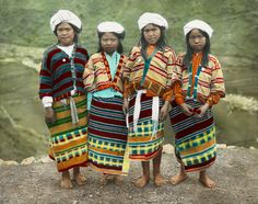 four women in native clothing standing on the edge of a cliff overlooking a body of water