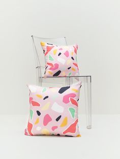 two colorful pillows sitting on top of each other next to a white chair and table