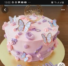 a pink cake with butterflies on it sitting on top of a wooden table next to the words happy birthday