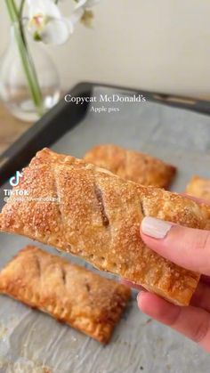 a person is holding up some food on a baking sheet with flowers in the background