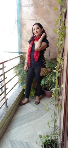 a woman in black shirt and red scarf standing next to potted plants on balcony