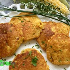 four crab cakes on a white plate with parsley sprigs and corn in the background