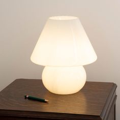 a white lamp sitting on top of a wooden table next to a pen and paper