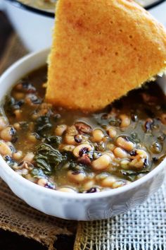 a white bowl filled with beans and spinach next to a piece of pita bread