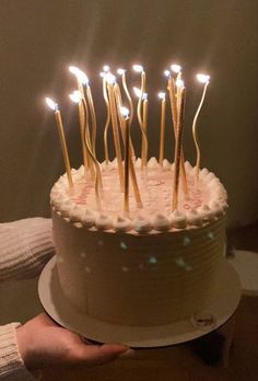 a cake with white frosting and lit candles on it is being held by a person