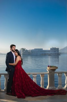 a man and woman in formal wear standing on a balcony overlooking the water with a cruise ship in the background