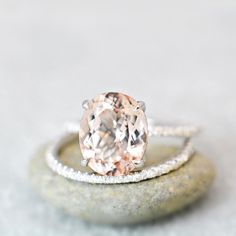 an oval shaped pink diamond ring on top of a rock with sparkles around it