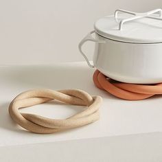 a white pot and two wooden rings sitting on top of a table next to each other