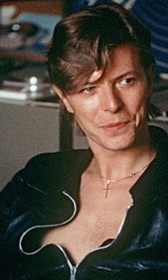 a woman wearing a black leather jacket sitting in front of a computer desk and looking at the camera