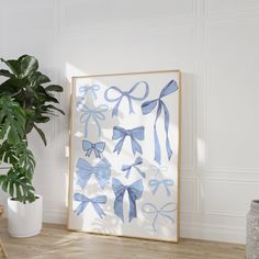 a painting with blue bows on it next to a potted plant in a white room