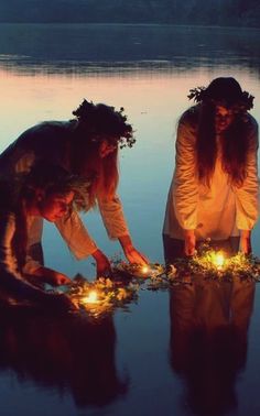 two women lighting candles in the water at night with their reflection on the water's surface