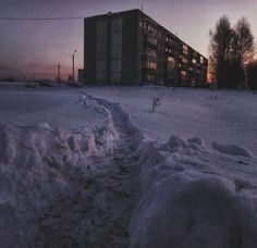 a snow covered path in front of a building at dusk with the sun going down