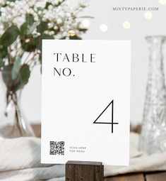 a table number sign sitting on top of a wooden block next to a vase with flowers