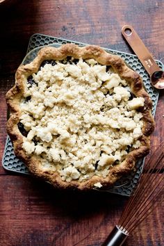 a pie sitting on top of a wooden table next to a whisk and utensil