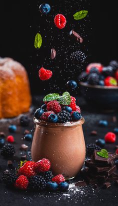 chocolate pudding with berries and mint sprinkles falling out of it on a black surface