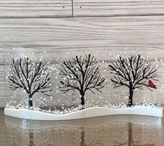 a glass block with three trees and a red bird on the branch, in front of a wood background