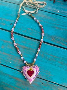 Handcrafted and adorned with beads, this lovely pink heart is accompanied by a string of matching beads and crystals. The leather straps allow for customizable wear, making this necklace a versatile addition to any outfit. Adjustable Colorful Beads Necklace For Valentine's Day, Adjustable Pink Heart Necklaces, Adjustable Pink Heart-shaped Necklaces, Pink Adjustable Heart-shaped Necklace, Heart-shaped Colorful Beads Jewelry For Valentine's Day, Valentine's Day Heart-shaped Jewelry With Colorful Beads, Valentine's Day Heart-shaped Colorful Beads Jewelry, Colorful Heart-shaped Beaded Jewelry, Handmade Heart-shaped Jewelry For Festivals