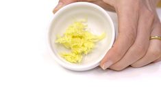 a person holding a white bowl with yellow food in it's palm and hands