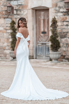 a woman in a white wedding dress is standing outside with her back to the camera