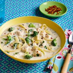 a yellow bowl filled with pasta and broccoli on top of a blue table cloth