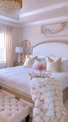 a white bed sitting in a bedroom next to a chandelier and two windows