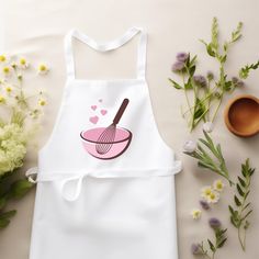 a white apron with a whisk and hearts on it next to some flowers