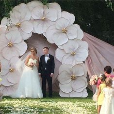 a bride and groom are standing in front of a large flower arch at their wedding