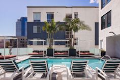 an empty swimming pool with lounge chairs and palm trees in front of the apartment building