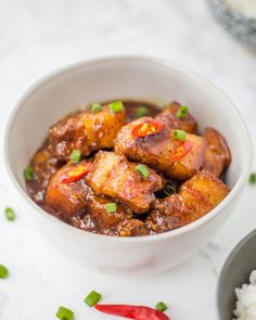 a white bowl filled with food on top of a table next to rice and red peppers