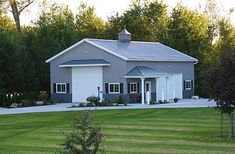 a large gray house sitting in the middle of a lush green field next to trees