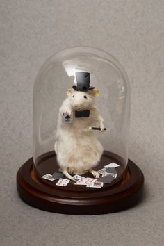 a mouse in a top hat and bow tie under a glass dome with playing cards underneath