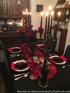 a dining room table is set with black and red plates, silverware and candles