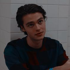 a young man sitting in front of a white tiled wall