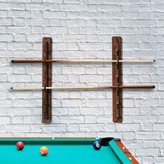 a pool table with cues and balls on it next to a white brick wall,