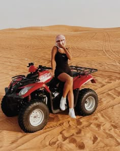 a woman sitting on top of an atv in the middle of sand dunes, talking on her cell phone