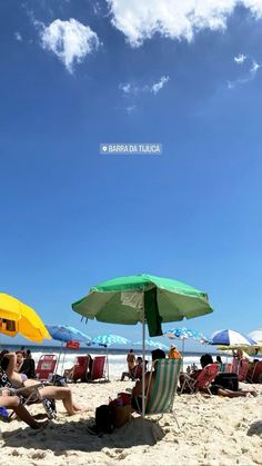 people sitting under umbrellas at the beach on a sunny day with blue skies and white clouds