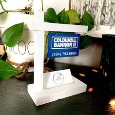 a white clock sitting on top of a wooden table next to a potted plant