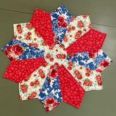 a red, white and blue flowered table topper on a green surface with flowers