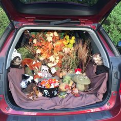 the trunk of a red car with stuffed animals and plants in it's trunk