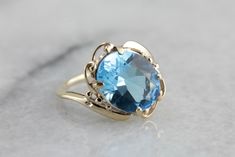 This vintage gold mounting is simple with decorative, sweeping shoulders on the sides and secure prongs. This piece is set with a modern, blue topaz. The color of this stone is deeper, a rich, almost turquoise water color. This would make a lovely cocktail ring, and is also a sturdy enough stone to wear everyday! Metal: 10K Yellow Gold Gem: Blue Topaz 4.46 Carats Gem Measurements: 11.9 x 9.8 mm, Oval Ring Size: 4.25 Classic Blue Topaz Solitaire Ring, Formal Blue Solitaire Topaz Ring, Formal Blue Topaz Solitaire Ring, Elegant Blue Topaz Ring In 14k Gold, Blue Topaz Solitaire Ring For Formal Occasions, Blue Topaz Birthstone Ring For Formal Occasion, Elegant Turquoise Topaz Gemstone Ring, Vintage Blue Topaz Ring In 14k Gold, Elegant Turquoise Topaz Birthstone Ring