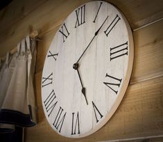 a large clock mounted to the side of a wooden wall with roman numerals