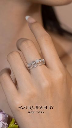 a woman's hand with a wedding ring on her finger and flowers in the background