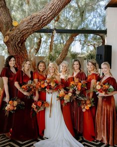 a group of women standing next to each other holding bouquets in front of a tree