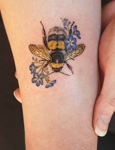 a woman's arm with a tattoo of a bee and flowers on the side