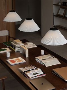 three lamps hanging over a wooden table with books and coffee cups on top of it