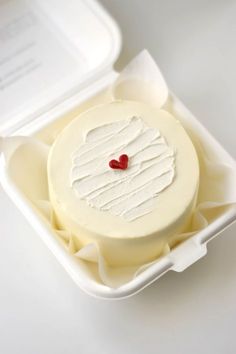 a white cake in a plastic container with a red heart on it