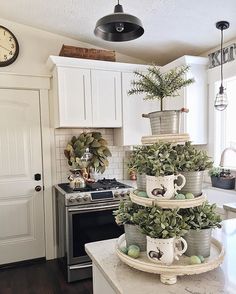 a kitchen with white cabinets and green plants on the top of two tiered trays