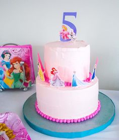 there is a pink cake with princess figures on it and other decorations around the cake