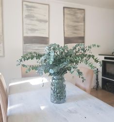 a vase filled with green leaves sitting on top of a white table next to a fireplace